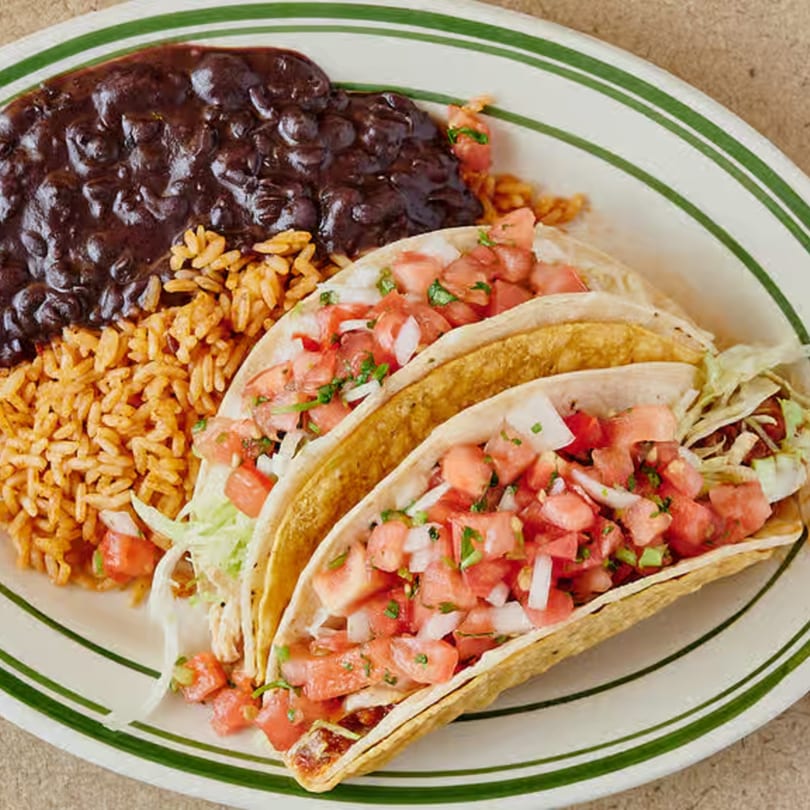 Two tacos with rice and black beans on a white plate with green stripes.