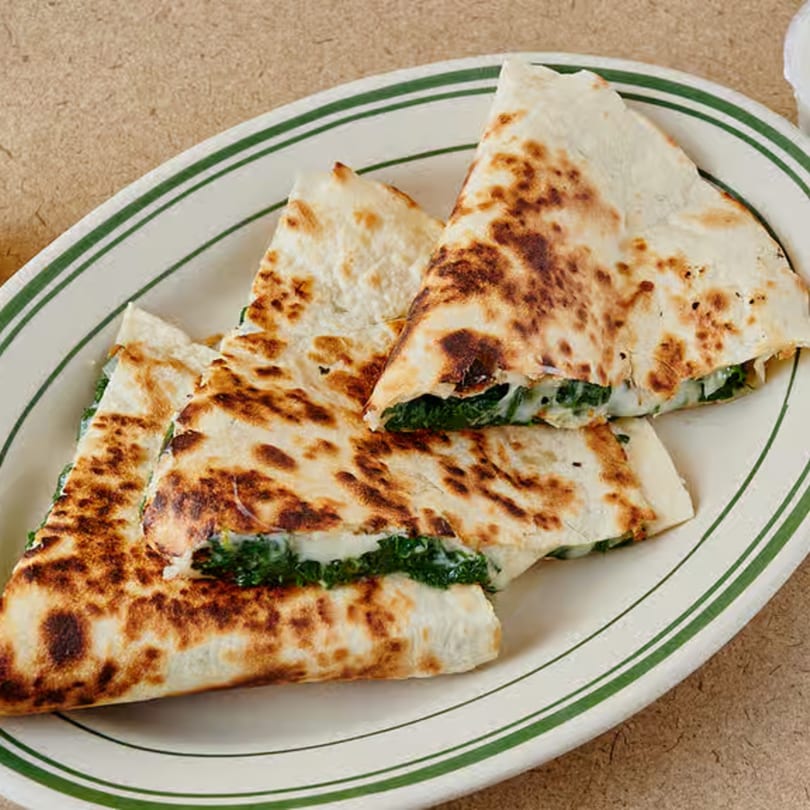 Four triangular quesadilla pieces with melted cheese and green filling on a white plate with green stripes.