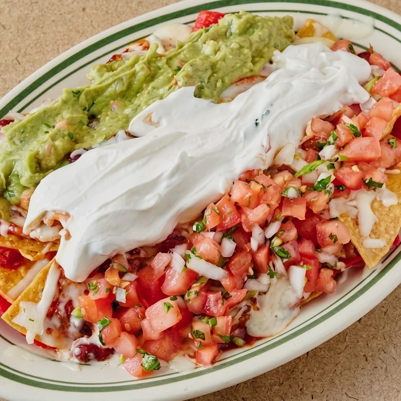 A platter of nachos topped with guacamole, sour cream, pico de gallo, and melted cheese.