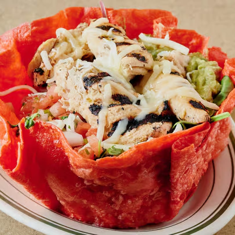 Grilled chicken taco salad in a vibrant red tortilla bowl with guacamole and pico de gallo.