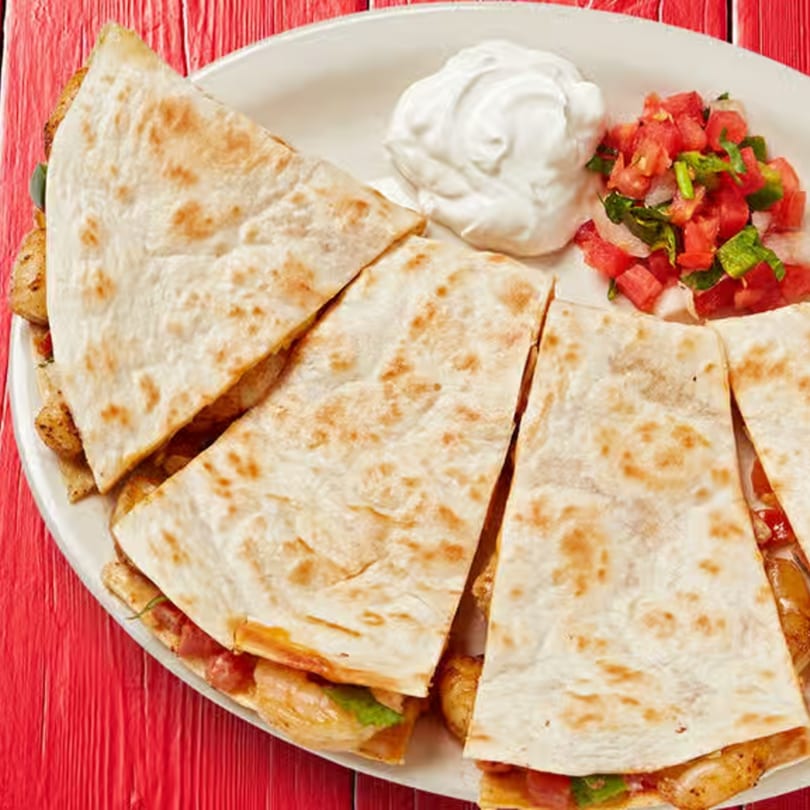 Chicken quesadillas with pico de gallo and sour cream on a white plate.