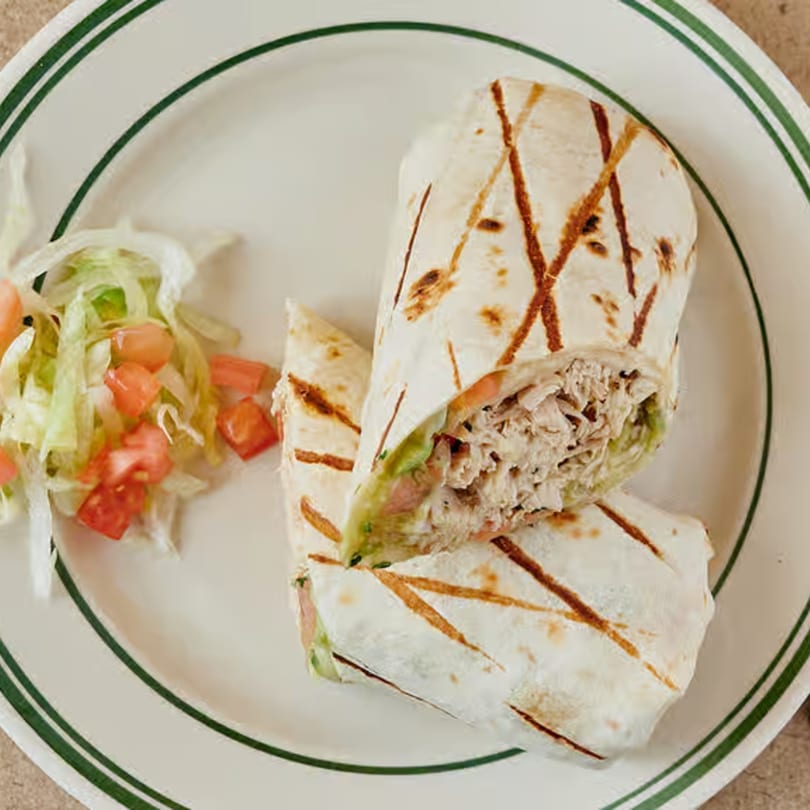 Two grilled chicken wraps with shredded lettuce and diced tomatoes on a white plate with green stripes.